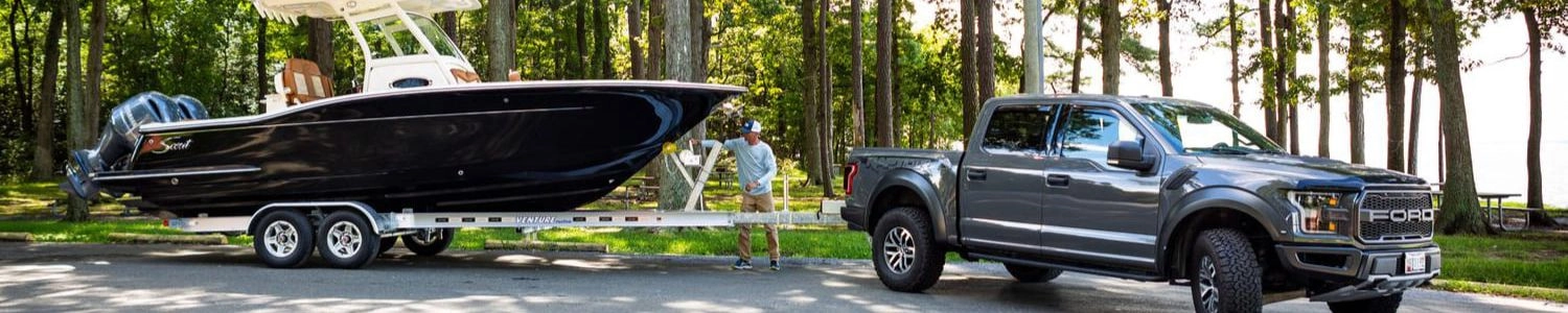 A gray Ford truck towing a large black boat on a trailer